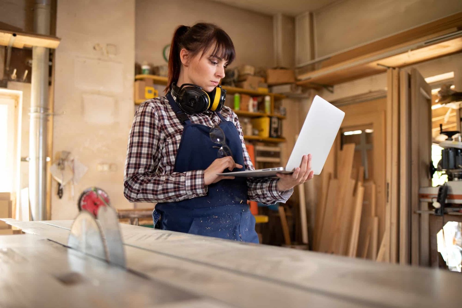Carpenter woman using laptop with blueprints and planning work in her carpentry workshop artisan femme site internet