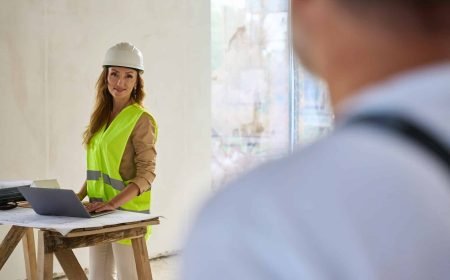 Builder looking at realtor standing near table with laptop Builder looking at realtor standing near table with laptop