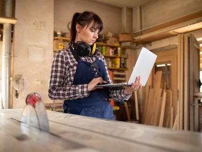 Carpenter woman using laptop with blueprints and planning work in her carpentry workshop artisan femme site internet