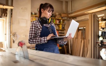 Carpenter woman using laptop with blueprints and planning work in her carpentry workshop artisan femme site internet