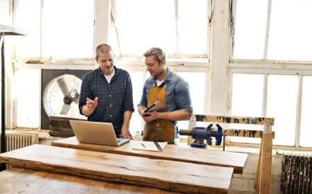 Male Carpenters Looking At Laptop And Discussing In Workshop Male Carpenters Looking At Laptop And Discussing In Workshop